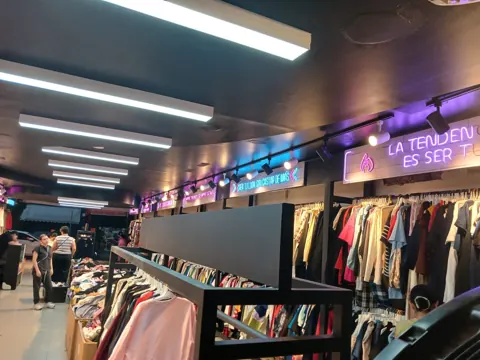 Vista amplia del interior de Outlet de 99 con exhibidores de ropa y letreros de neón