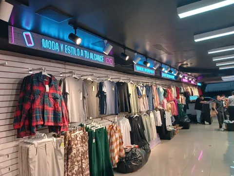 Pasillo interior de Outlet de 99 con prendas de hombre y mujer bajo letreros de neón