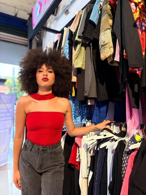 Modelo con top rojo junto a un rack con prendas surtidas dentro de Outlet de 99